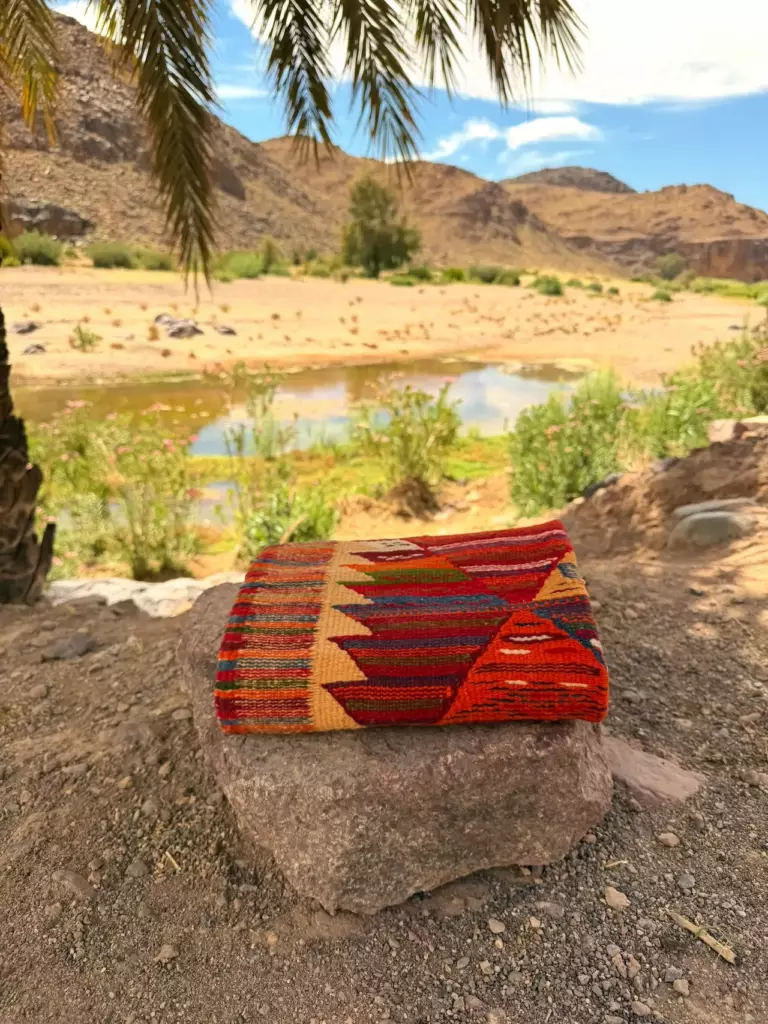 Amazigh kilim rug folded on rock, oasis, Southern Morocco